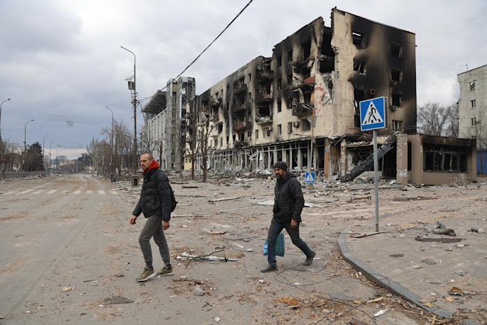 Two men pass a burned-out building amid debris-filled streets in the city of Mariupol.