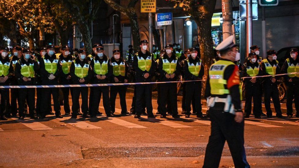 Wearing fluorescent jackets and face masks, a row of police officers stand watch behind a cordon